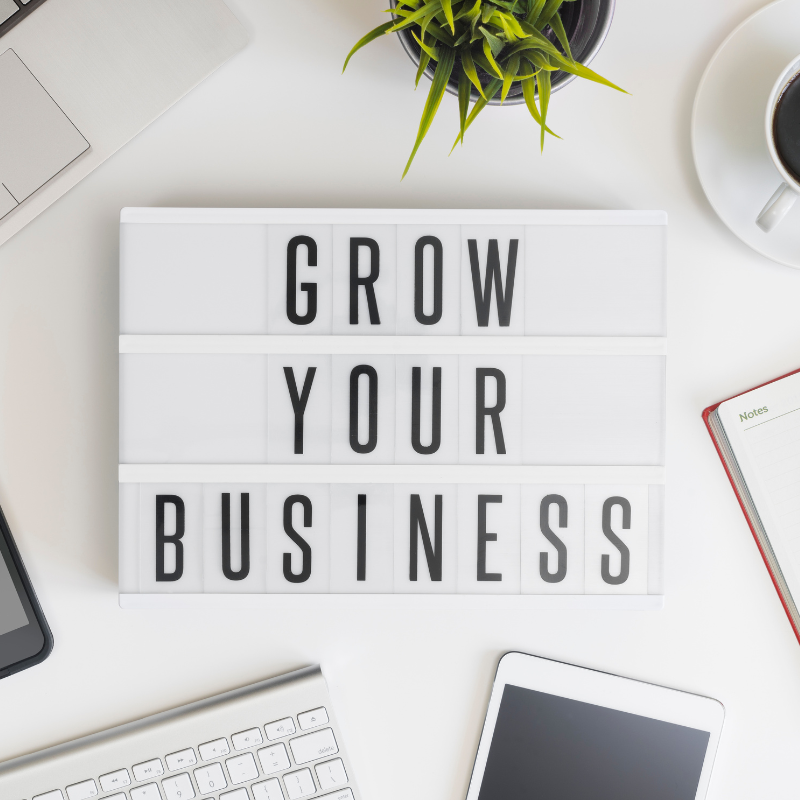 white sign on a desk with the black words 'Grow Your Business'.