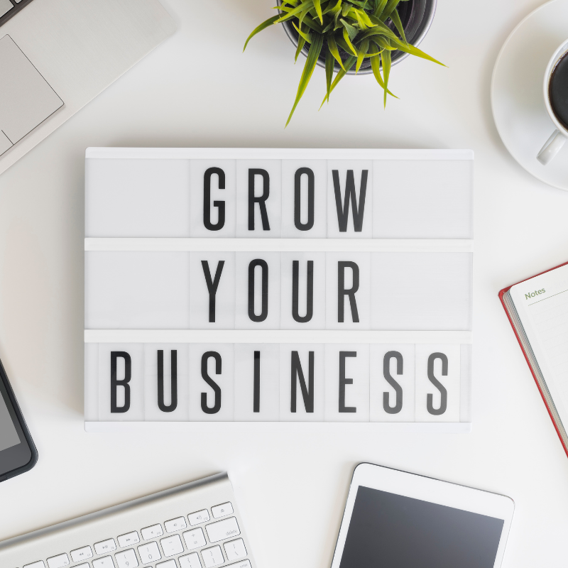 white sign on a desk with the black words 'Grow Your Business'. 